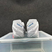 Rear view of white and gray Nike basketball shoes with blue heel lettering and patterned gray outsoles