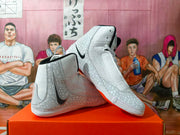 Angled view of two white and gray Nike high-top sneakers with patterned panels, black accents, and orange outsole details.