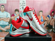 Angled view showing the silver upper, red swoosh, red collar, and layered basketball sneaker construction.
