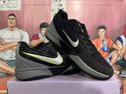 Angled view of the black and gray Nike sneakers showing the side swoosh, padded collar, lace-up construction, and gray outsole.