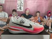 Side profile of a white Nike GT sneaker with a black Swoosh, peach and pink sole accents, and a speckled midsole.