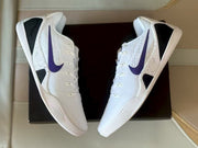 Pair of white and purple Nike Kobe 9 sneakers shown from the side over a black shoebox.