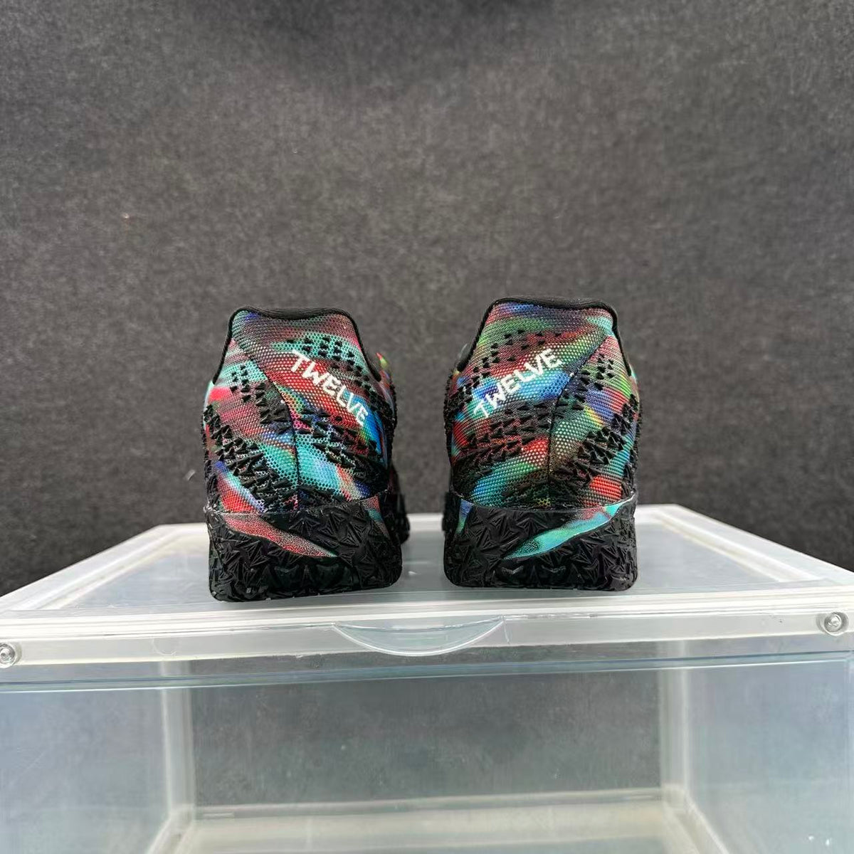 Rear view of black sneakers with a multicolor patterned upper and textured black soles.