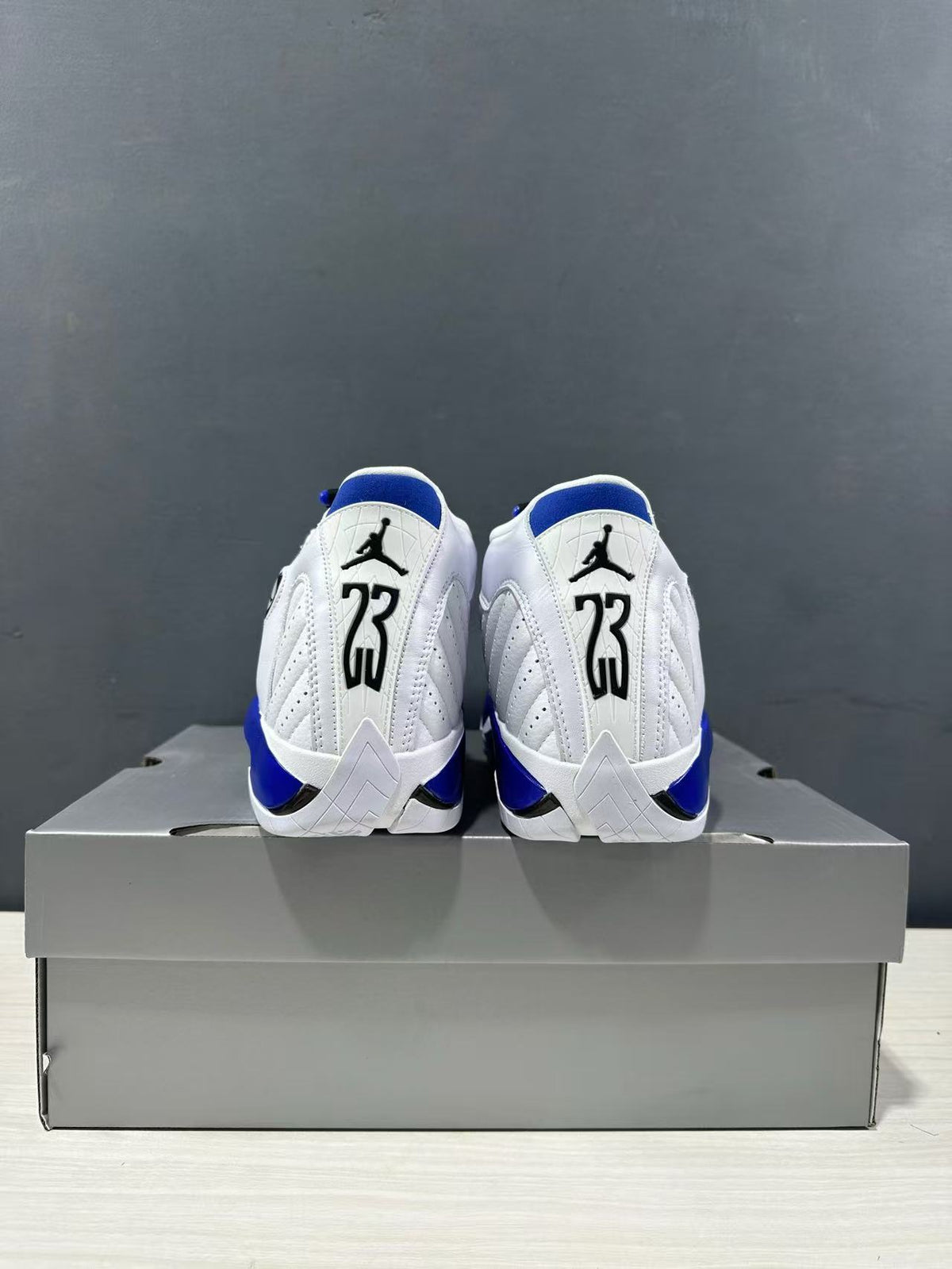Rear view of the white and blue Jordan Air Jordan 14 sneakers placed on a gray shoe box.