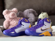 Pair of matching purple, silver, and gold high-top sneakers photographed against a teddy bear background.