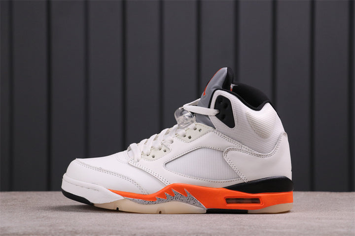 Side view of a white, black, and orange Jordan high-top sneaker with an orange-and-black midsole and visible air unit.