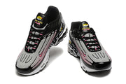 Front angled view of the pair of black, white, and pink Nike Air Max Plus sneakers.