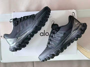 Pair of black Alo hiking sneakers shown at an angle against a branded box, highlighting the side panels and rugged soles.