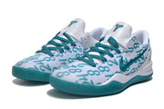 Pair of white Kobe 8 sneakers with teal graphic lettering, teal laces, and teal outsoles.