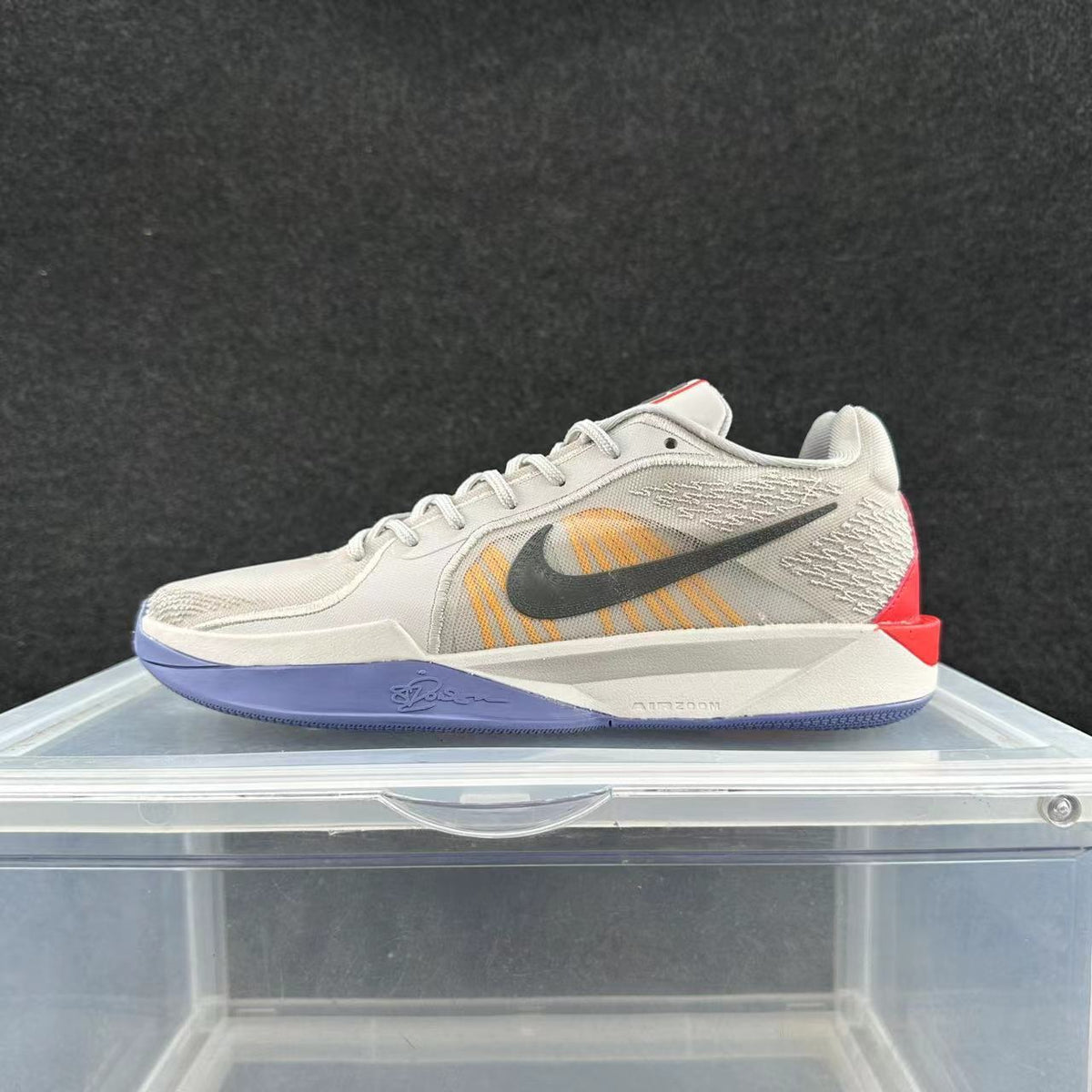 Side view of an off-white Nike low-top basketball shoe with orange accents, a dark Swoosh, purple outsole, and red heel detail.