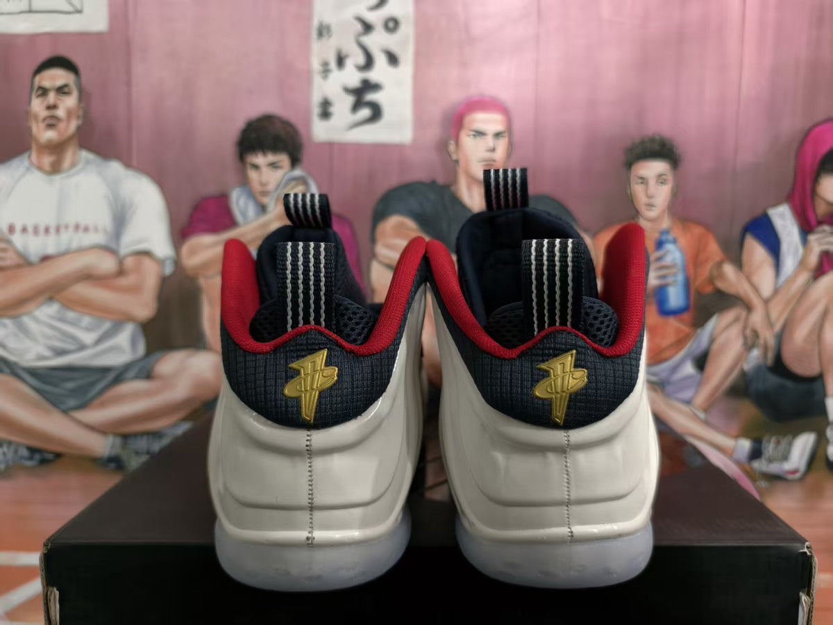 Rear view of white, navy, and red Nike Air Foamposite One sneakers with gold-tone heel emblems.