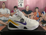 Side view of a white Nike basketball sneaker with a purple Swoosh, yellow heel accent, black side insert, and ribbed outsole.