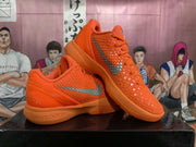 Angled view of two orange Nike basketball sneakers displaying the textured panels, silver Swoosh details, and Nike branding on the outsole.