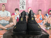 Front view of black high-top basketball sneakers with gold tongue and side accents on a shoebox.