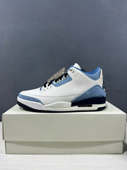 Side profile of one sneaker showing the white upper, blue trim, and visible heel cushioning window.