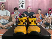 Front view of yellow and black Nike sneakers with yellow laces and perforated toe panels, displayed on a black box.