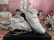 Angled view of the white, black, and gold high-top basketball sneakers displayed together, showing the straps, gold side branding, and translucent-looking soles.