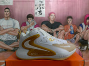 Side profile of a white Nike basketball sneaker with yellow-gold overlays, visible Zoom text, and a gum-colored outsole.
