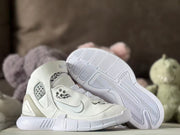 White sneakers displayed with one outsole facing upward, showing the patterned traction surface.