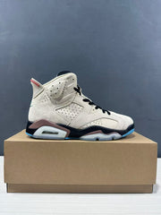 Side profile of the high-top sneaker displayed on a shoebox, highlighting the cream upper, black midsole, and blue outsole edge.