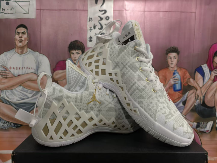 Pair of white and light gray Jordan basketball sneakers with geometric side overlays and gold accents, displayed on a black box.
