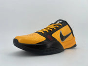 Angled front view of an orange-and-black low-top shoe with yellow-orange laces.