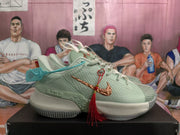 Side view of pale green Nike basketball sneakers with textured panels, copper-colored Swooshes, blue hang tags, and red tassel decoration.