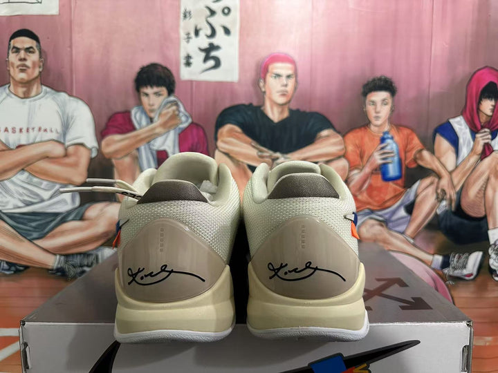 Rear view of white Nike basketball sneakers showing Kobe-style heel signatures, padded collars and light-colored midsoles on a shoebox.