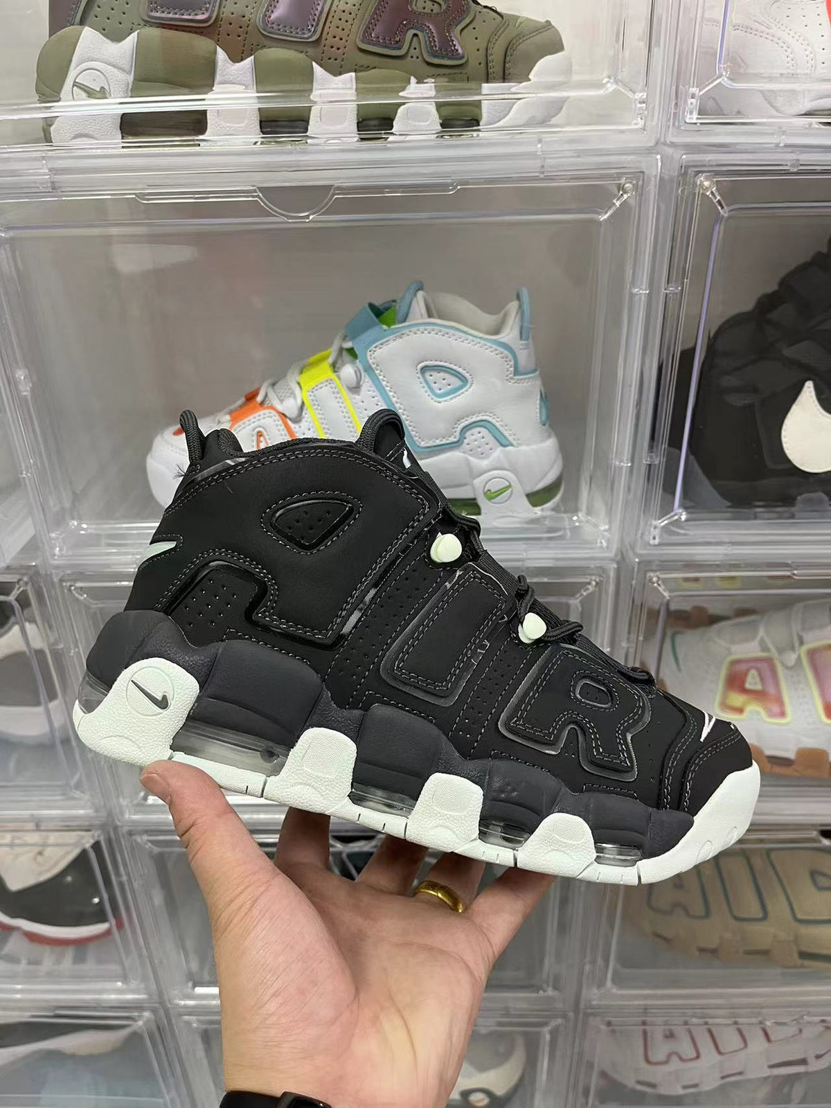 Black high-top sneaker with prominent AIR lettering, a visible Nike swoosh, off-white outsole sections, and green-gray accent details, photographed in a display case.