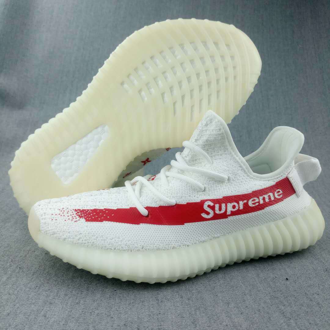 White low-top sneaker with a red side stripe, visible “Supreme” lettering, patterned upper, and translucent ribbed sole.