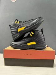 Pair of black and yellow Jordan Air Jordan 12 Retro sneakers arranged on a Jordan shoebox, showing the side panels and outsole edges.