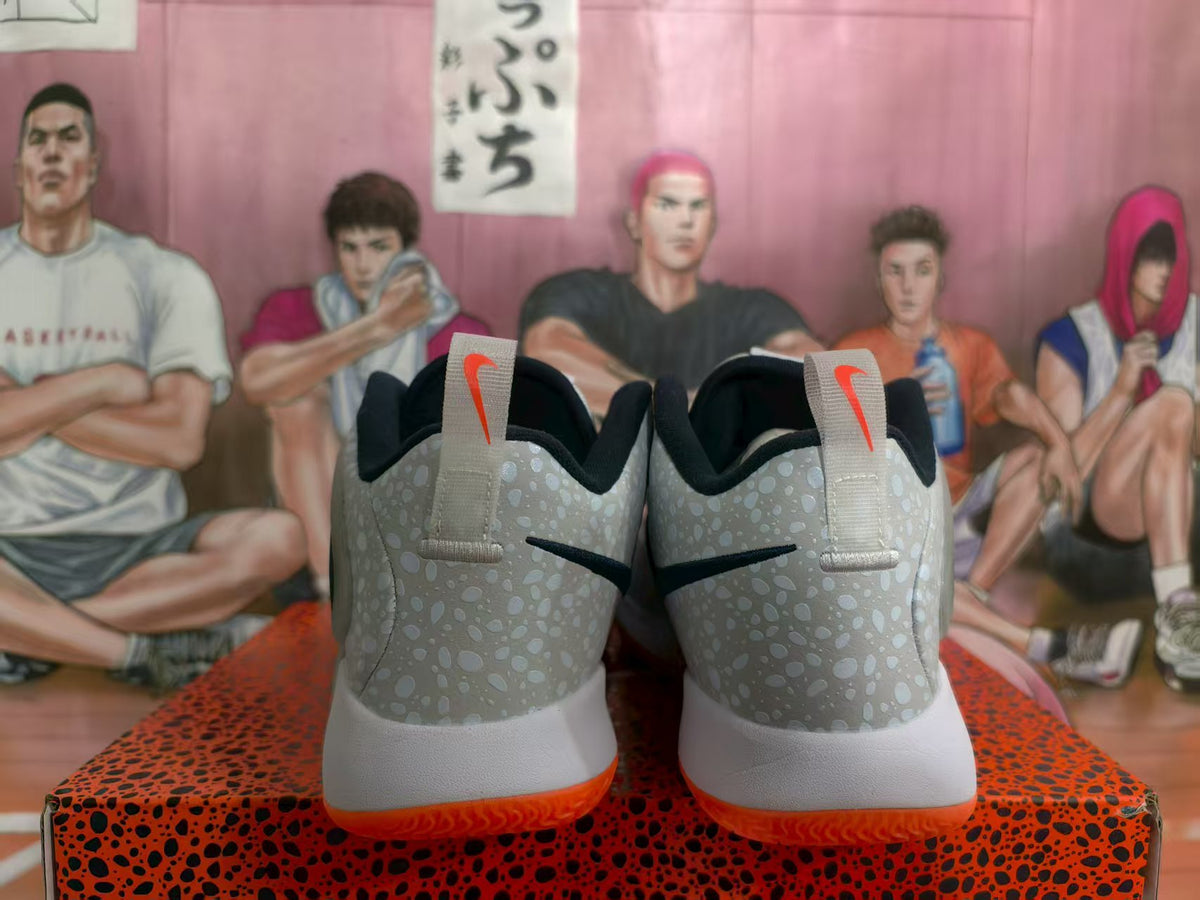 Rear view of white Nike basketball sneakers with speckled gray heel panels, black branding, and orange outsoles.