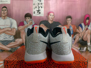 Rear view of white Nike basketball sneakers with speckled gray heel panels, black branding, and orange outsoles.