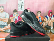 Angled side view showing black sneakers with patterned toe overlays and red outsole accents.