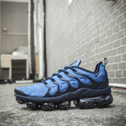 Blue and black Nike Air VaporMax Plus sneaker in an outdoor side view.