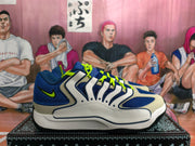 Side profile of a blue, white, and light gray Nike sneaker with neon green swoosh