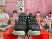 Front view of black Nike basketball sneakers showing layered uppers, lace-up closures, light toe accents, and grey-green details.