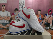 Angled view of two white Nike low-top sneakers displaying red side and heel accents with blue outsole detailing.
