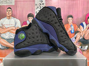 Angled view of a pair of black and purple Jordan basketball sneakers displayed on a shoebox.