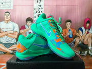 Pair of bright green-blue Nike basketball-style sneakers with orange and blue splatter accents, shown from an angled side view.