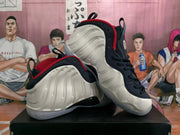 Two white, navy, and red Nike Air Foamposite One sneakers shown at an angle.
