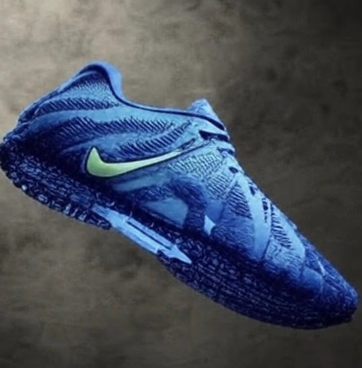 Blue low-top sneaker shown at an angle, featuring a visible Nike Swoosh, textured upper, padded collar, and patterned outsole.