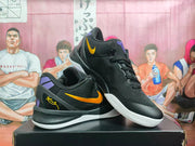 Angled view of the pair showing black uppers, purple details, gold Swooshes, and textured white outsoles.