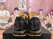 Rear view of the black sneakers showing glossy heel panels, yellow outsole accents, and signature-style heel graphics.