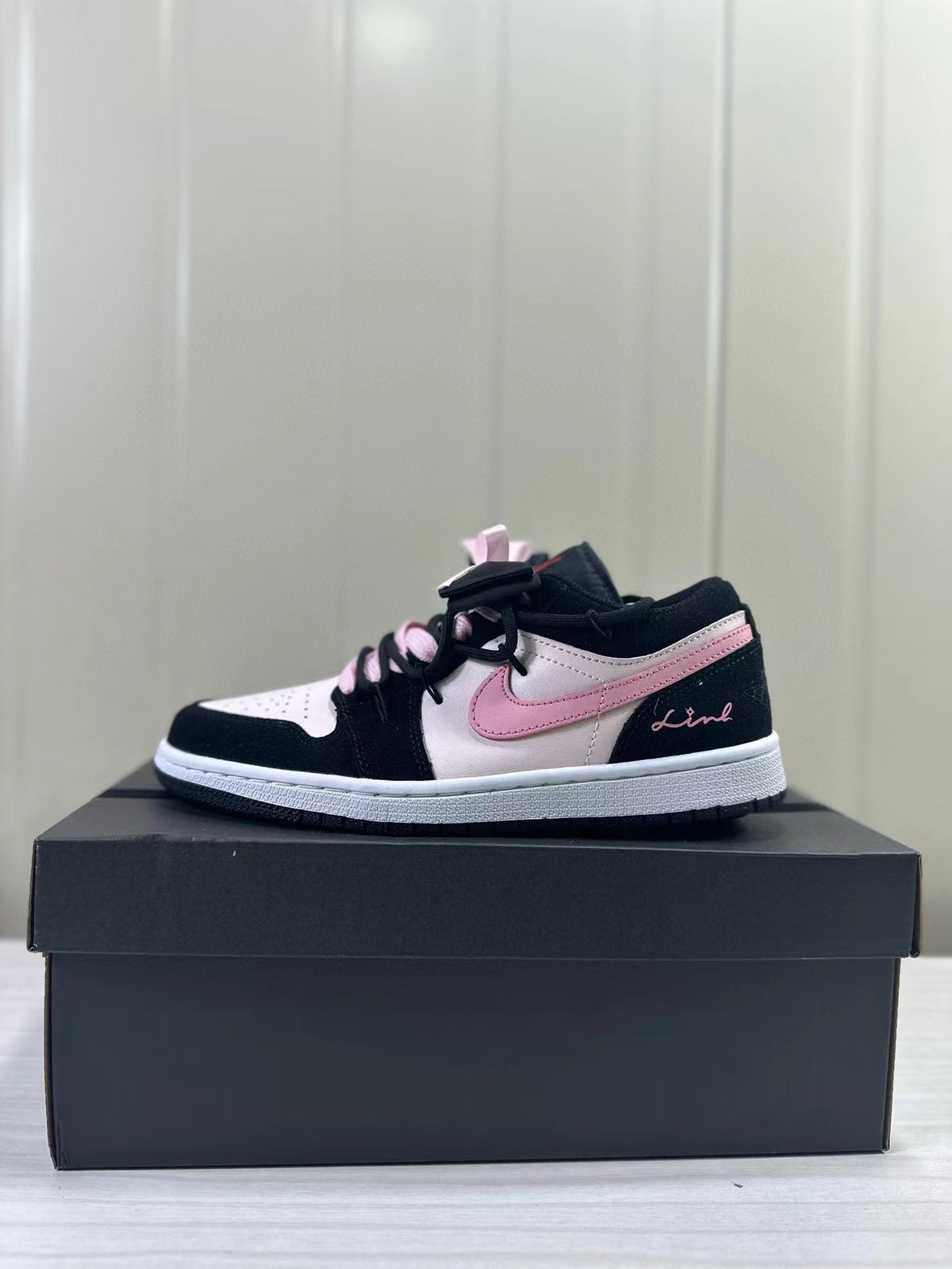 Black, pale pink, and white low-top sneaker shown in profile on a box