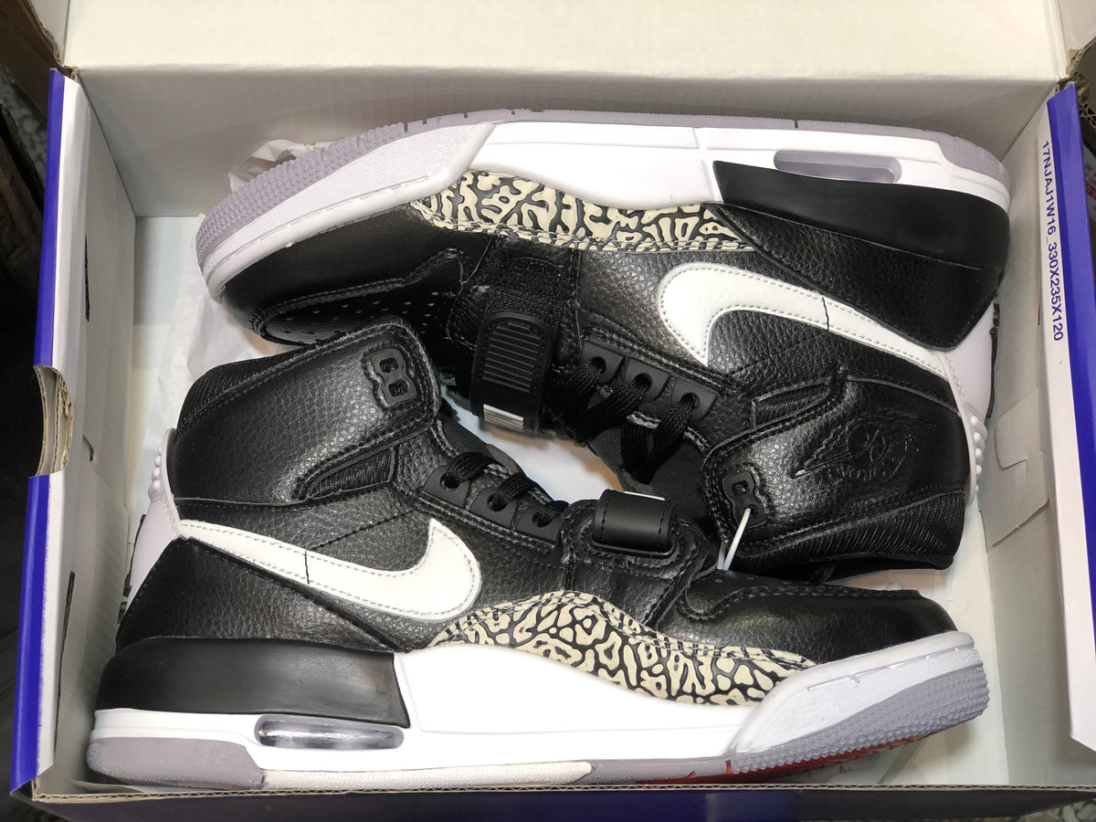Pair of black and white high-top sneakers shown inside a shoe box, featuring elephant-print panels and white Swooshes.