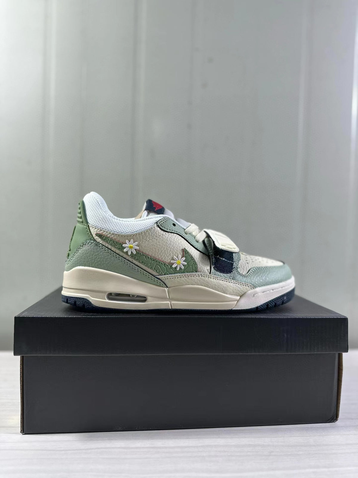 Side view of mint green and white low-top Jordan sneakers with daisy side details on a black shoebox.