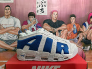 Side profile of a white and blue Nike sneaker showing layered white overlays, blue textile panels, perforations, and the segmented sole.