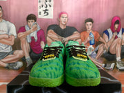 Front view of the green sneaker pair showing black laces, yellow-green lace details, and textured toe panels.