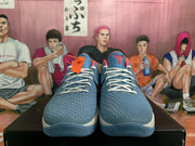 Front view showing the blue-grey textured uppers, white laces, orange-red tongue accents, and black-and-red tongue logos.